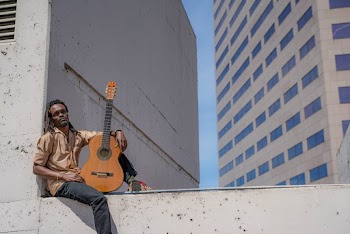 Selective Focus Photography of a Man in Brown Shirt Sitting on Concrete Slab  Holding Guitar