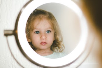 Selective Focus Photography of Girl Facing Lighted Magnifying Lamp