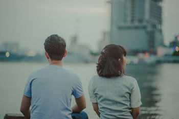 Selective Focus Photography of Man and Woman Watching Body of Water and Concrete Buildings