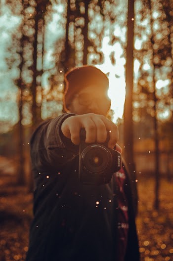 Selective Focus Photography of Man Holding Dslr Camera Near Trees
