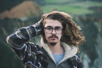 selective focus photography of man holding his hair wearing black and green zip-up hoodie and crew-neck shirt