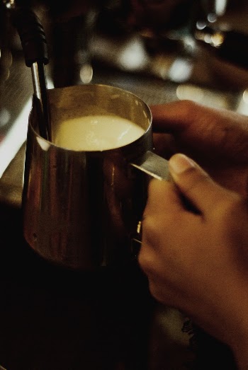 Selective Focus Photography of Person Holding Stainless Steel Mug with Milk Near Dispenser