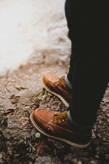 selective focus photography of person wearing brown lace-up shoes standing on rock