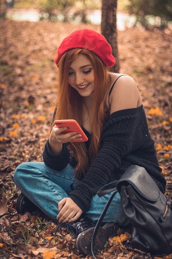 Selective Focus Photography of Sitting and Smiling Woman Using Smartphone