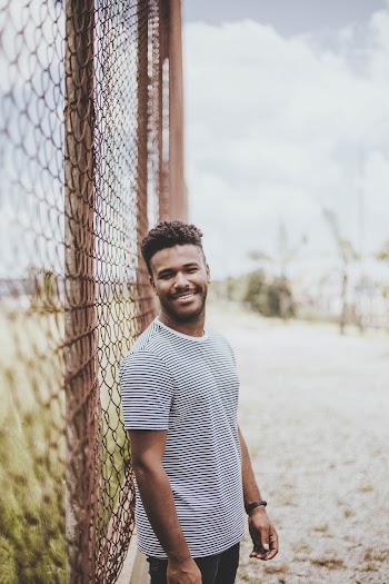 Selective Focus Photography of Smiling Man Standing Beside Fence