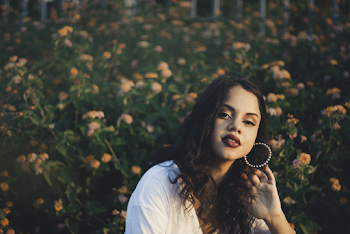Selective Focus Photography of Woman Holding Her Earrings Against Orange-petaled Flowers