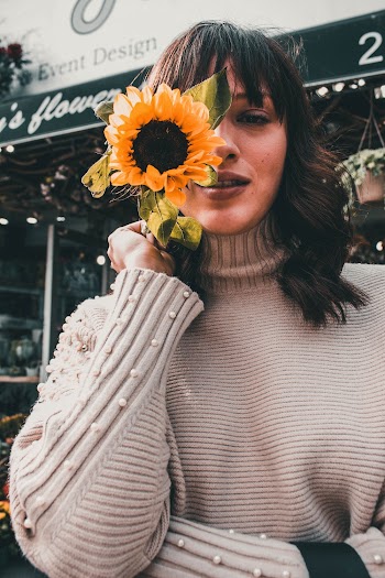 Selective Focus Photography of Woman in Gray Sweater Holding Yellow Sunflower Close To her Face