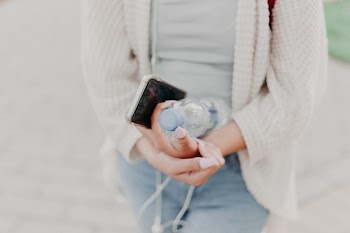 Selective Focus Photography of Woman in White Cardigan Holding Water Bottle and Black Smartphone