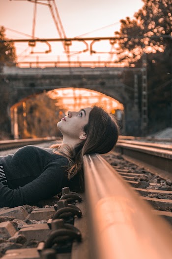 Selective Focus Photography of Woman Lying on Train Rail during Golden Hour