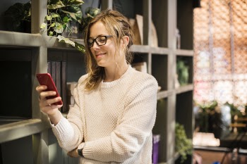 Selective Focus Photography of Woman Using Smartphone Beside Bookshelf