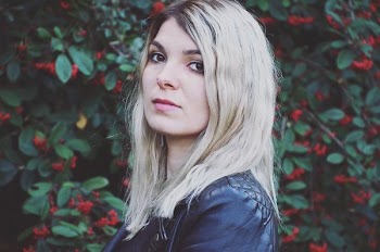 selective focus photography of woman with short blonde hair in front of red petaled flower