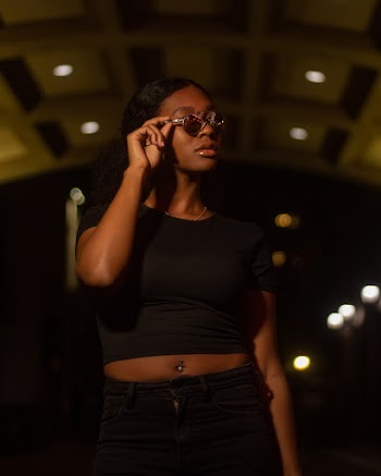 Selective Focus Woman in Black Crop Top, Sunglasses, and Black Jeans Posing While Looking Away