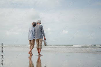 Senior couple holding hands and walking on the beach,other hand of the two was holding a pair of shoes.Plan life insurance at retirement concept.