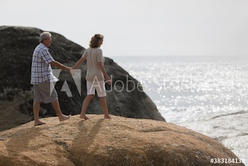 Senior couple holding hands on sunny beach rocks