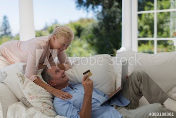 Senior couple online shopping with credit card and laptop on sofa