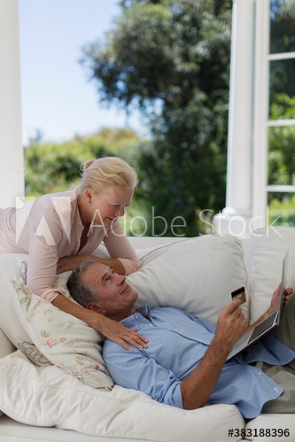 Senior couple online shopping with credit card and laptop on sofa