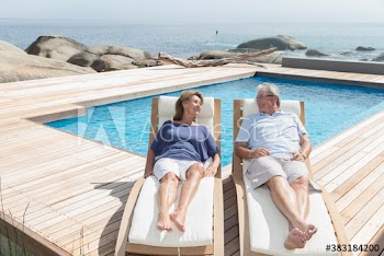 Senior couple relaxing on lounge chairs at sunny ocean poolside
