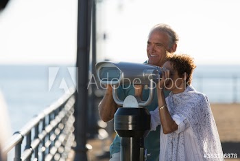 Senior couple using coin-operated binoculars on pier