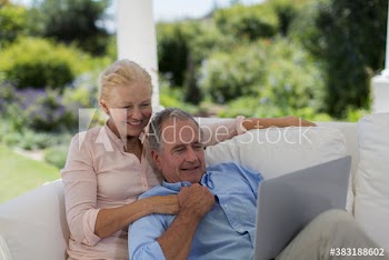 Senior couple using laptop on patio sofa