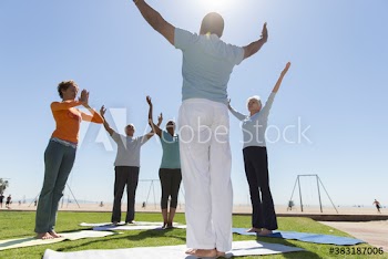 Senior friends practicing yoga on sunny beach lawn