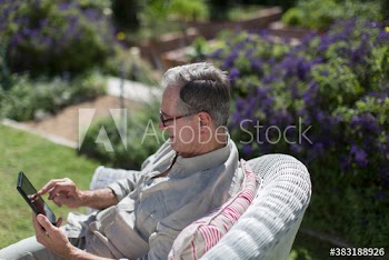 Senior man in wicker chair using digital tablet in sunny garden