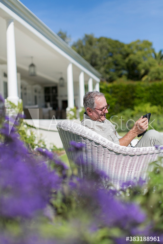 Senior man in wicker chair using digital tablet in sunny garden