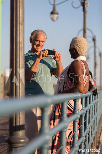 Senior man photographing wife on sunny pier