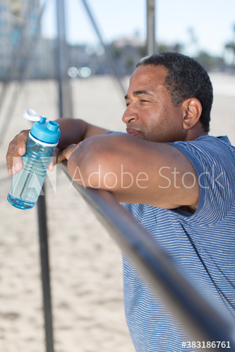 Senior man with water bottle resting from exercise on beach
