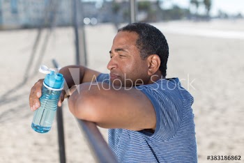 Senior man with water bottle resting from exercise on beach