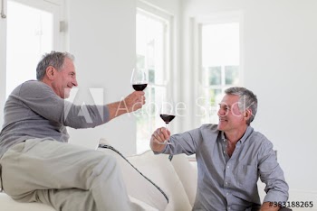 Senior men friends drinking red wine on sofa