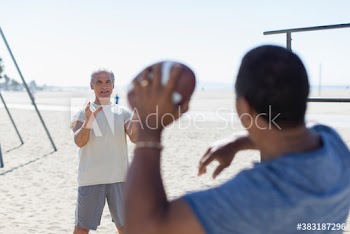 Senior men playing football on sunny beach