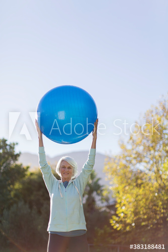 Senior woman exercising with fitness ball overhead in sunny park