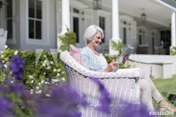 Senior woman in wicker chair using digital tablet in garden