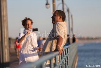 Senior woman photographing husband on sunny pier