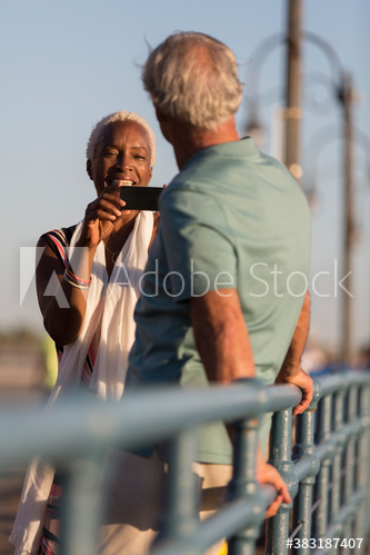 Senior woman photographing husband on sunny pier