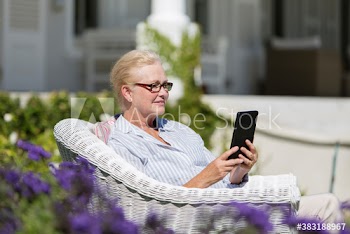 Senior woman using digital tablet in wicker chair in sunny garden