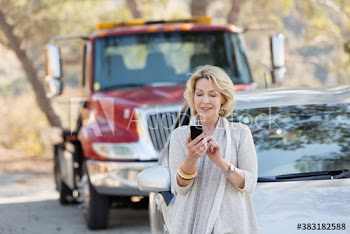 Senior woman with smart phone at roadside with car breakdown