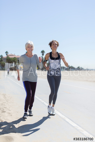 Senior women jogging on sunny beach boardwalk