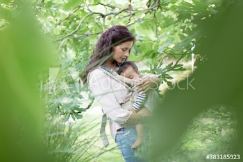 Serene mother holding baby son in carrier in lush garden