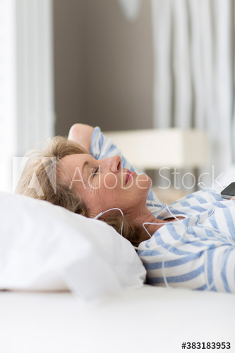 Serene senior woman listening to music with headphones on bed