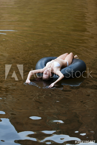 Serene young woman in bikini floating on inner tube on lake