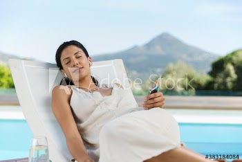Serene young woman relaxing and listening to music at poolside