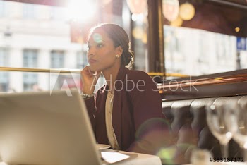 Serious businesswoman with laptop working in sunny restaurant