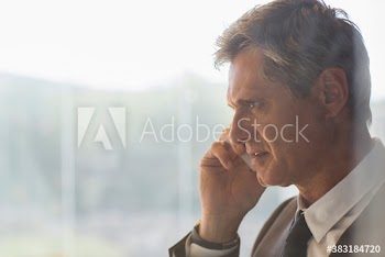 Serious corporate businessman talking on smart phone at window