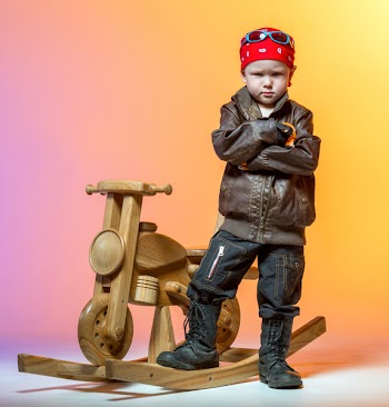 Serious little boy biker crossed his hands standing next to wooden...