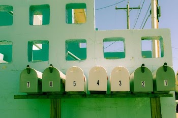 seven white and green mailboxes near white concrete wall