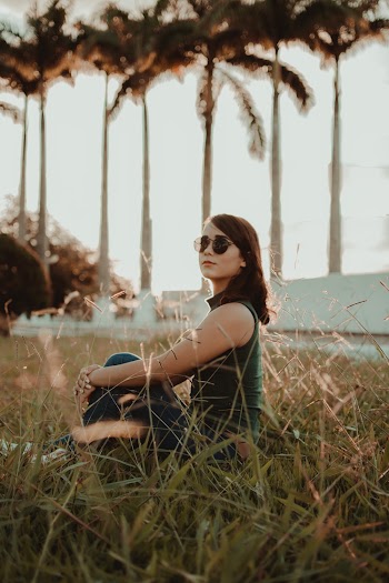 Shallow Focus Photo Of Woman In Green Sleeveless Shirt Sitting On Grass Field