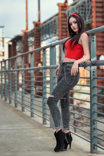 Shallow Focus Photo of Woman in Red Sleeveless Crop Top Leaning on Gray Fence