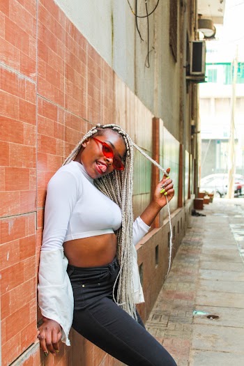 Shallow Focus Photo of Women in White Long-sleeved Crop Top Leaning on Brown Wall