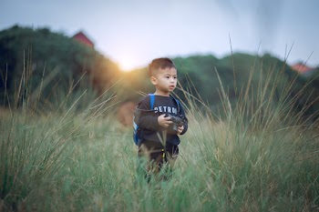 Shallow Focus Photography of Boy Standing on Green Grass Holding Camera